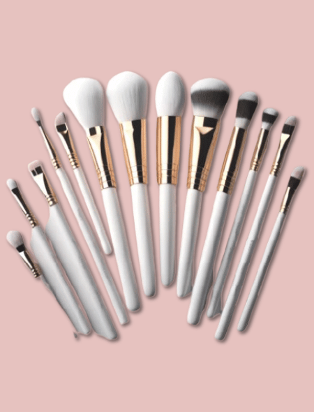 Set of twelve professional makeup brushes with white handles, gold ferrules, and soft gradient bristles in white, gray, and black, arranged in a fan shape.